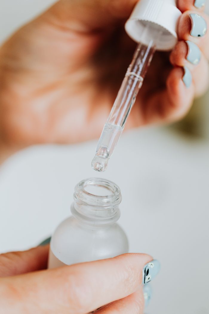 creative Hand holding a dropper, applying serum from a frosted glass bottle, close-up view.