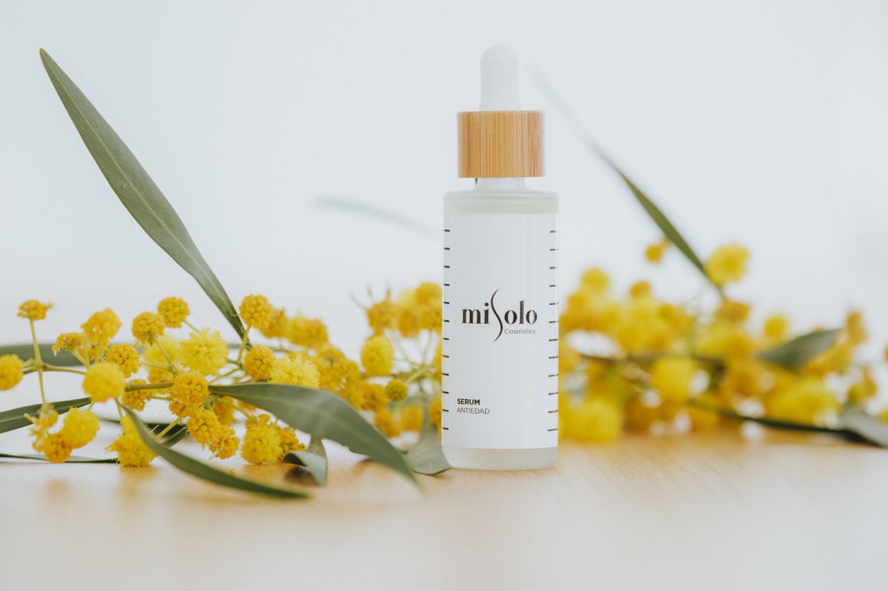 Services-02 Close-up of a cosmetic serum bottle with yellow flowers on a white background.